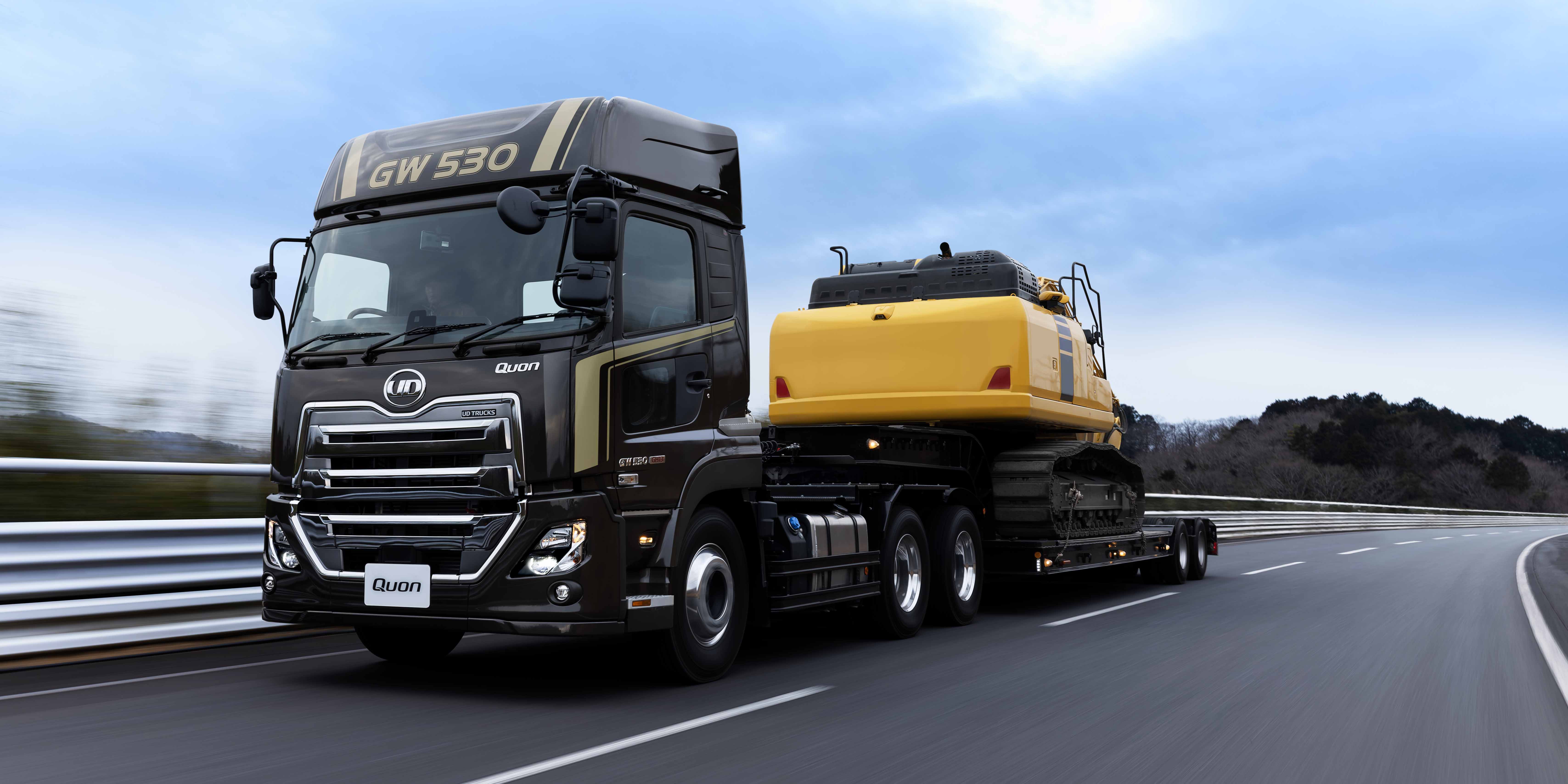 大型トラックが黄色い建設機械を載せて高速道路を走行