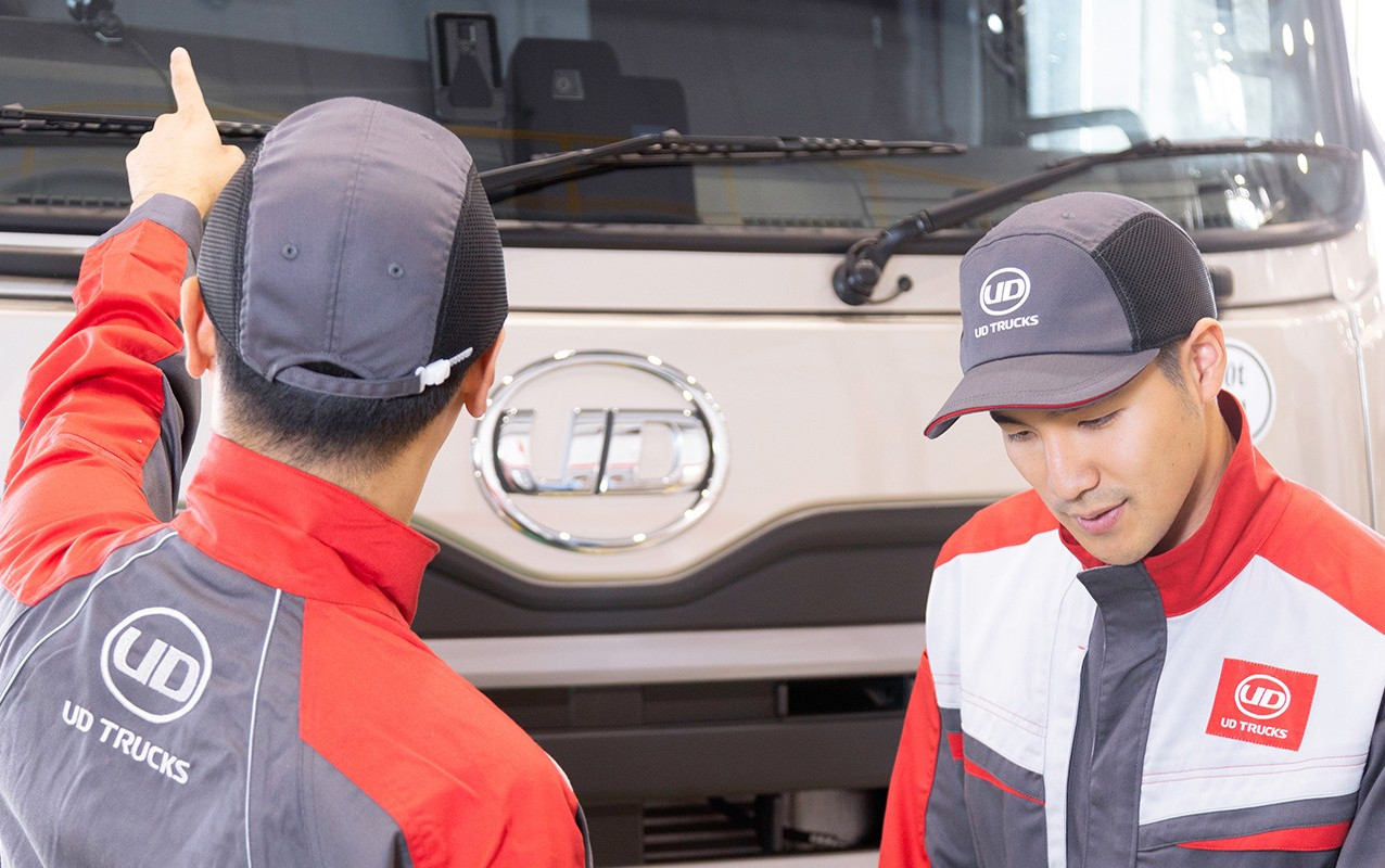 Two mechanics in uniforms inspecting a large truck, one pointing at the windshield.