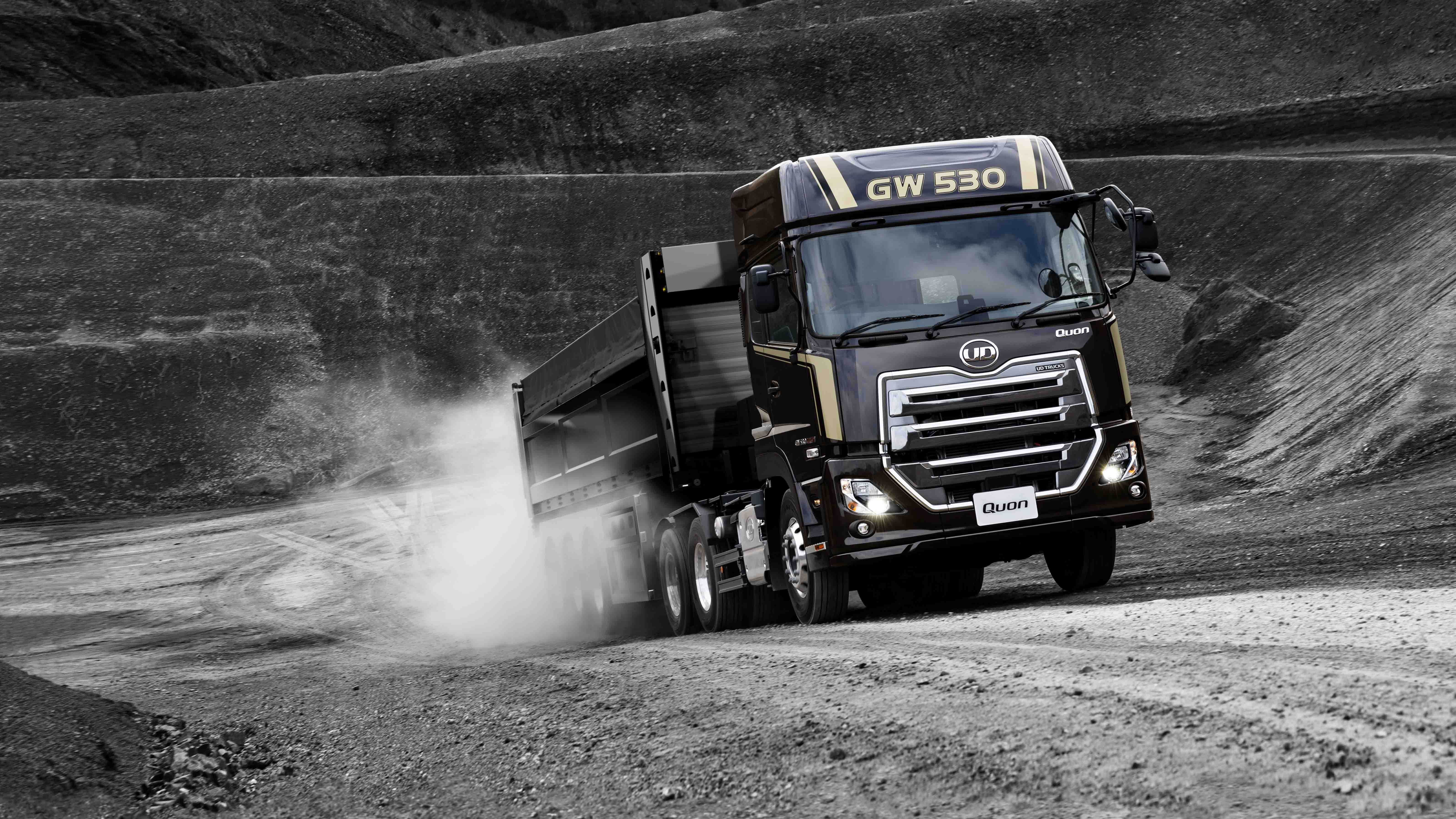 ダンプトラックが砂利道を走行し、砂ぼこりが舞っている。