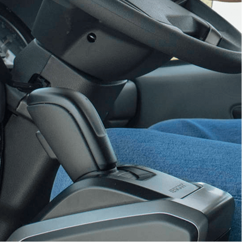 Motorcar gear shift lever next to steering wheel and blue trousers.