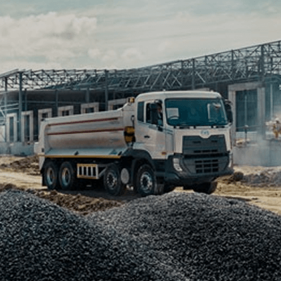 Truk besar di lokasi konstruksi dengan tumpukan kerikil di depan.