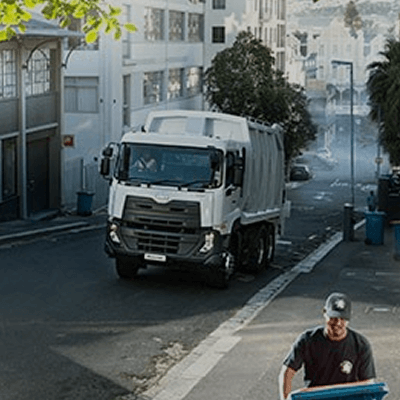 រថយន្តសំរាមស្ថិតនៅលើផ្លូវទីក្រុង; បុរសម្នាក់ទាញធុងសំរាម।