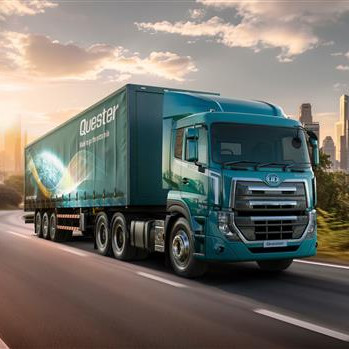 Lori ya samawati inaendesha barabarani, majengo marefu yakiwa mbali.