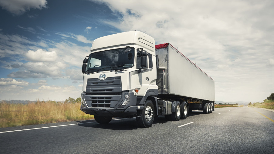 White semi-truck driving on a highway under a partly cloudy sky.