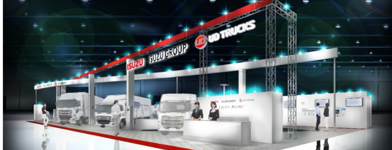 屋内展示会で大型トラック数台が照明の下に並ぶブース