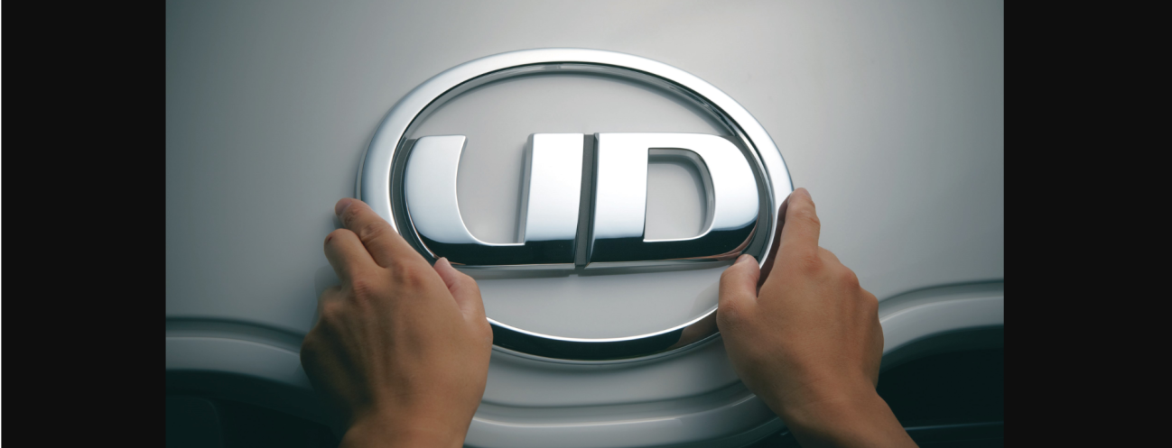 両手でUDロゴがついた車のエンブレムを触っている