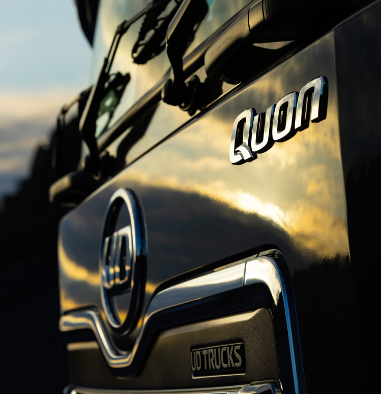 Shiny truck front with "Quon" emblem reflecting sunset sky.