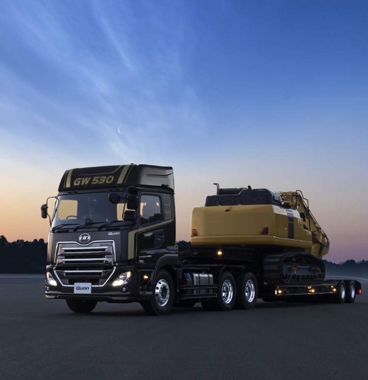 大きなトラックがショベルカーを運搬している夕暮れの道路