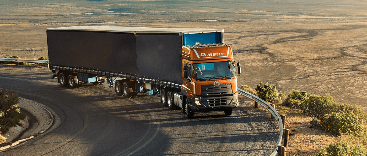 Orange na trak-trailer na lumiliko sa kalsada sa gitna ng disyerto.